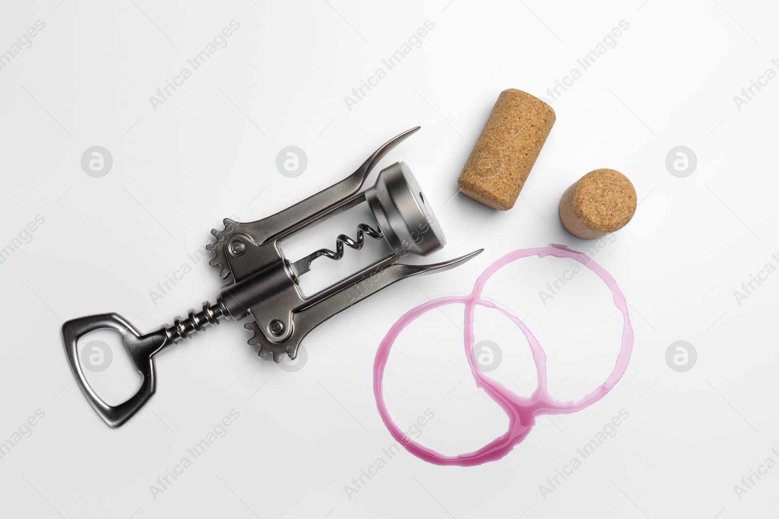 Photo of Wing corkscrew, corks and red wine stains on white background, top view