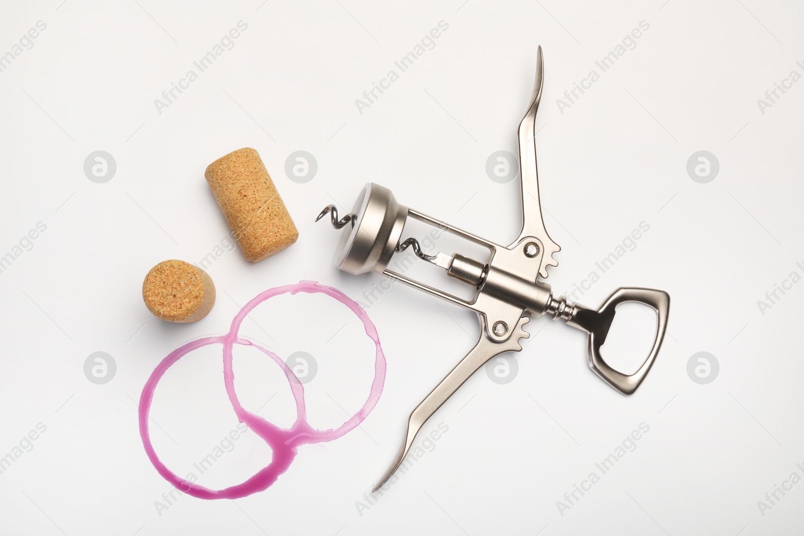 Photo of Wing corkscrew, corks and red wine stains on white background, top view