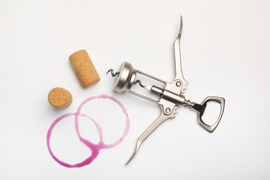 Wing corkscrew, corks and red wine stains on white background, top view