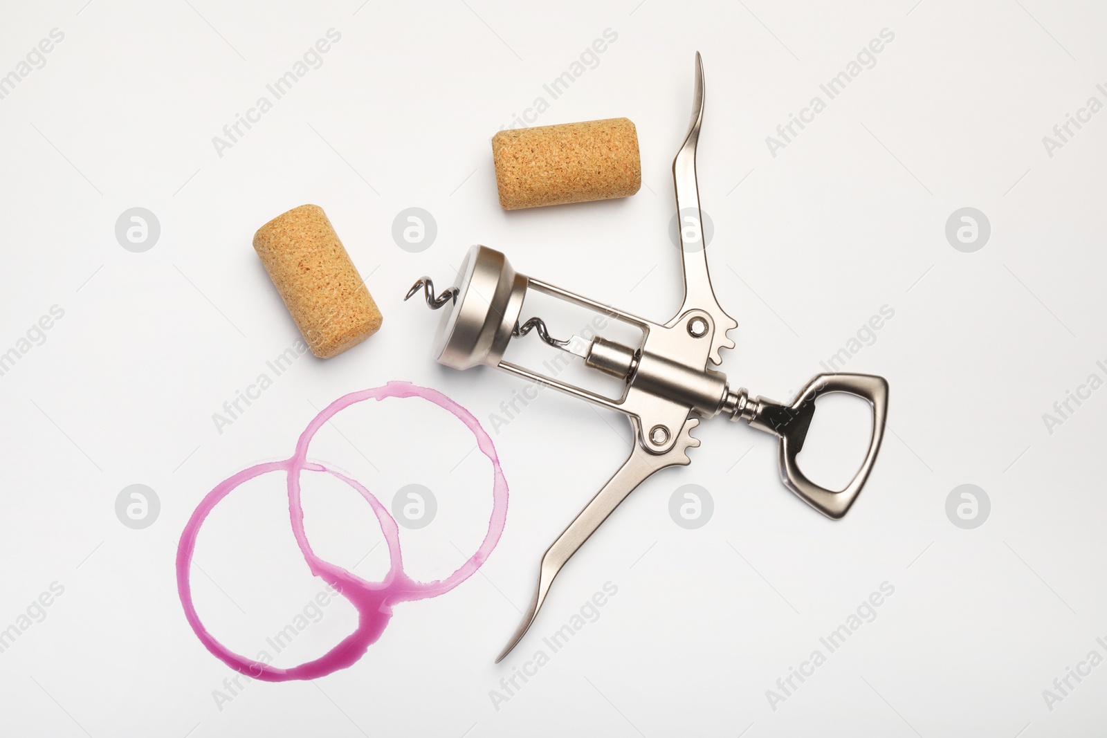 Photo of Wing corkscrew, corks and red wine stains on white background, top view