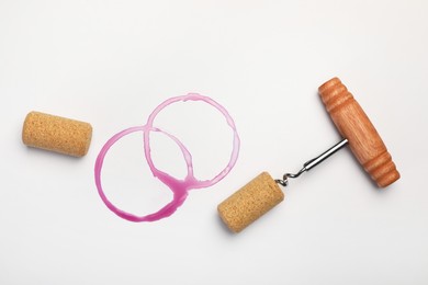 Corkscrew, corks and red wine stains on white background, top view