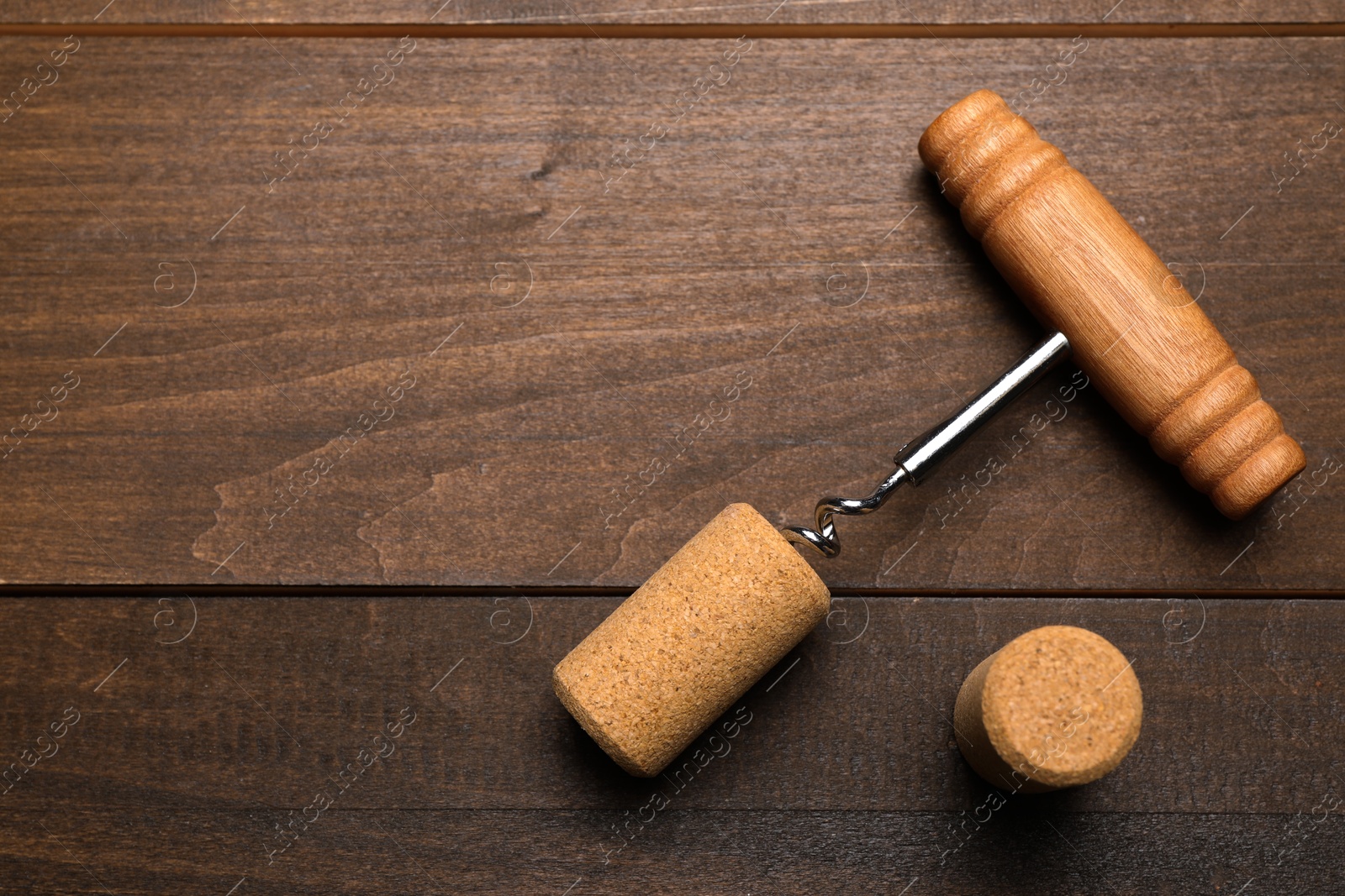 Photo of Corkscrew and corks on wooden table, flat lay. Space for text