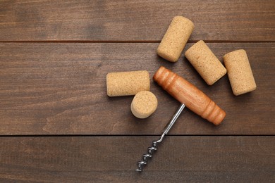 Photo of Corkscrew and corks on wooden table, flat lay. Space for text