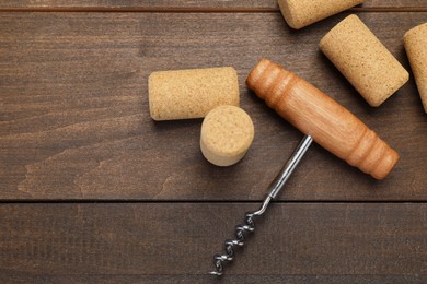 Photo of Corkscrew and corks on wooden table, flat lay. Space for text