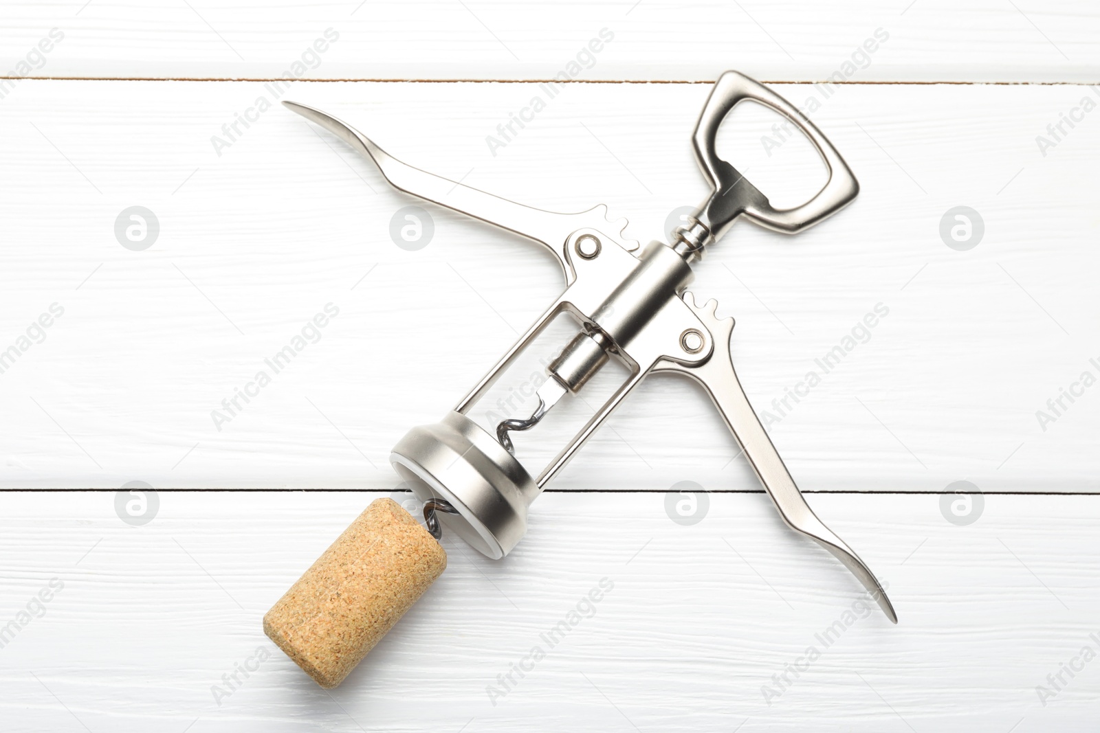 Photo of Wing corkscrew and cork on white wooden table, top view