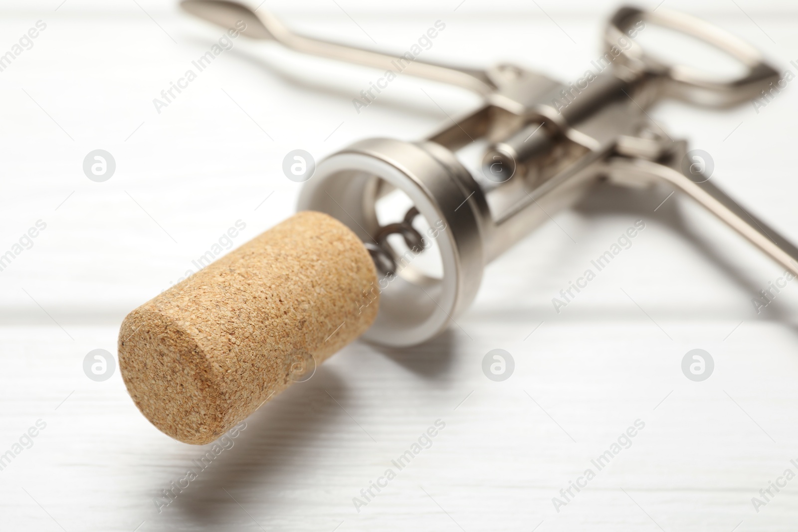 Photo of Wing corkscrew and cork on white wooden table, closeup