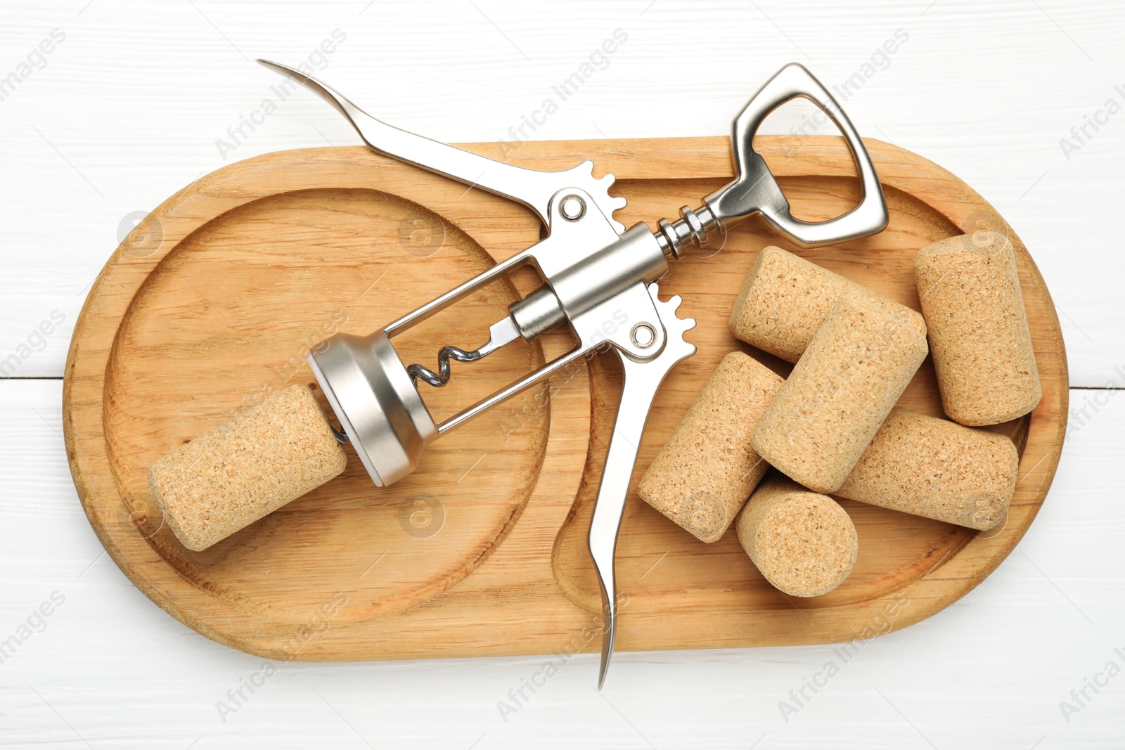 Photo of Wing corkscrew and corks on white wooden table, top view