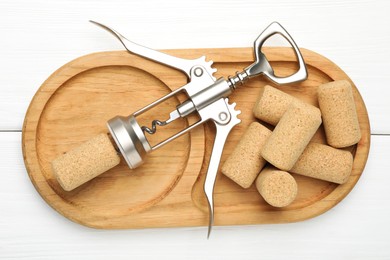 Wing corkscrew and corks on white wooden table, top view