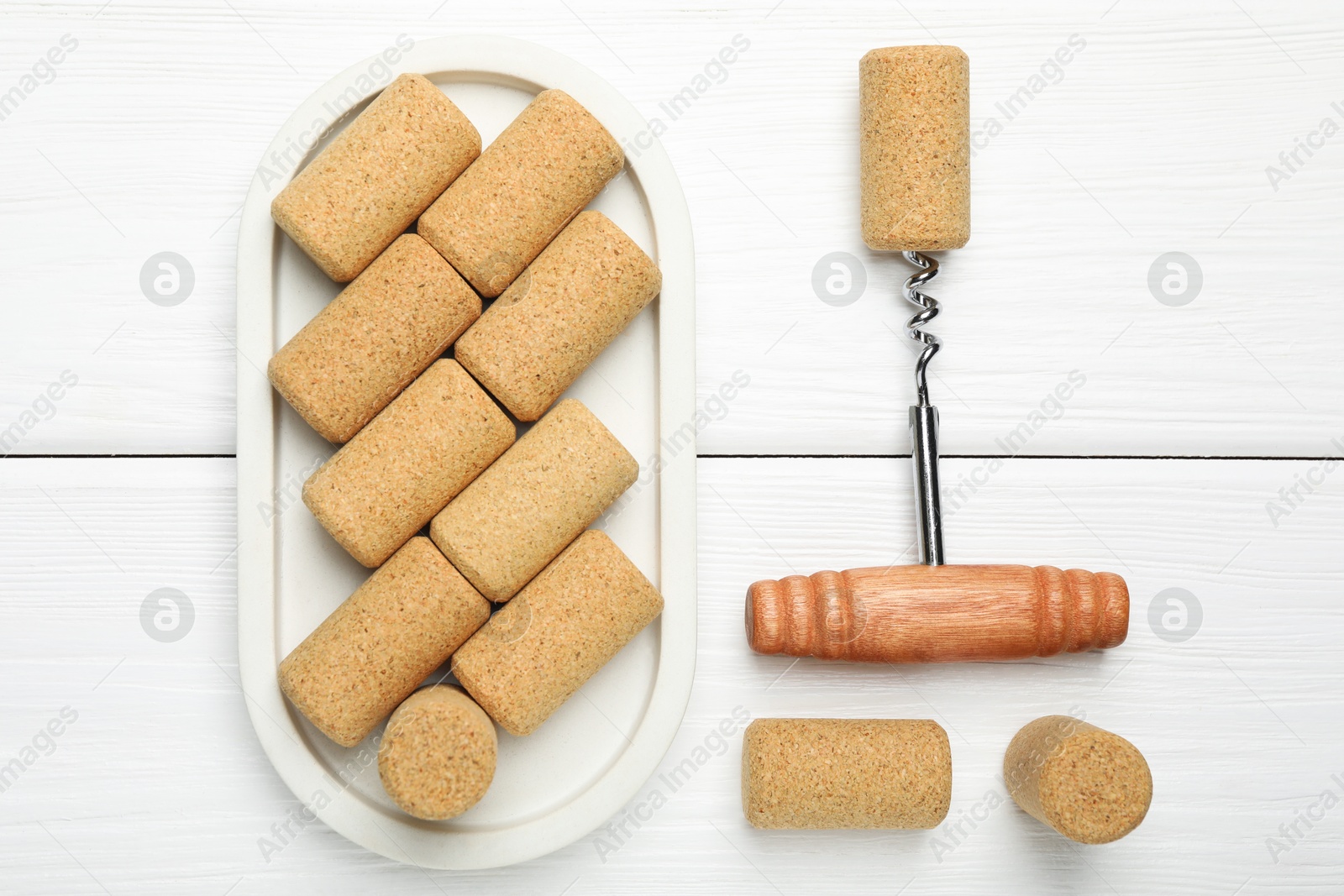 Photo of Corkscrew and corks on white wooden table, flat lay