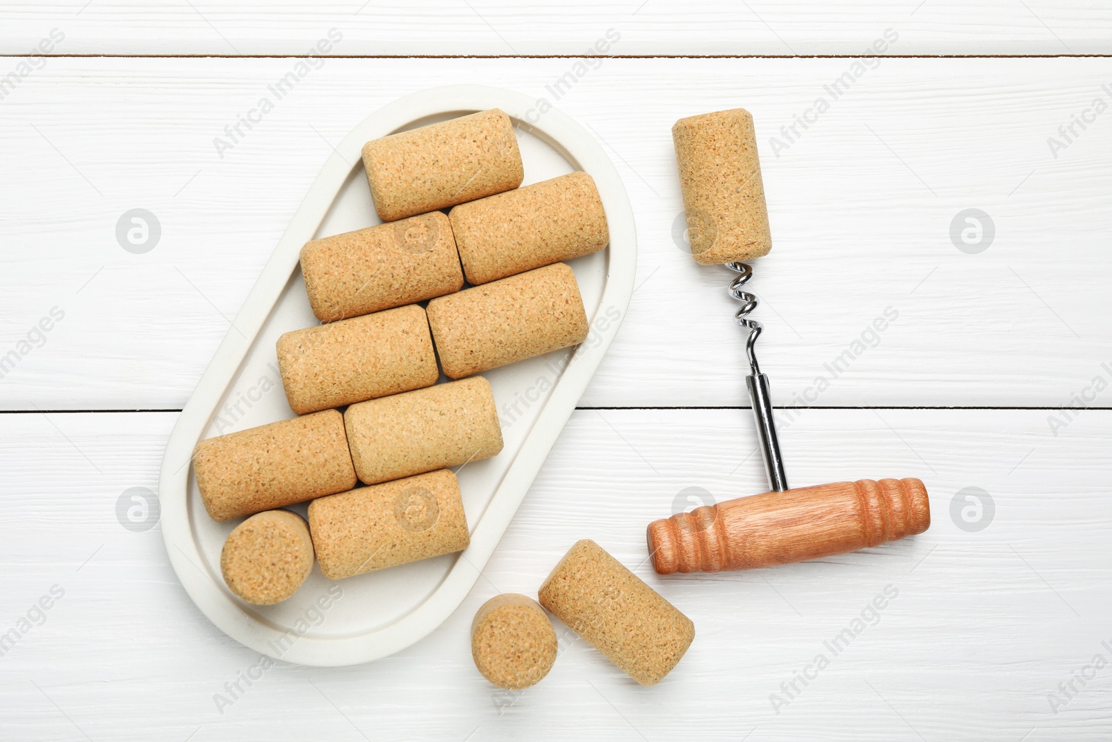 Photo of Corkscrew and corks on white wooden table, flat lay