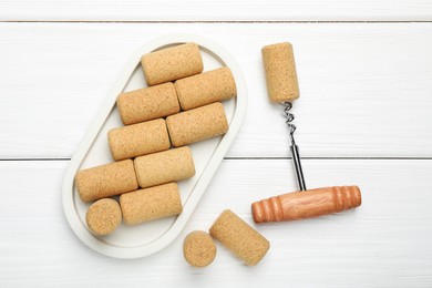 Corkscrew and corks on white wooden table, flat lay