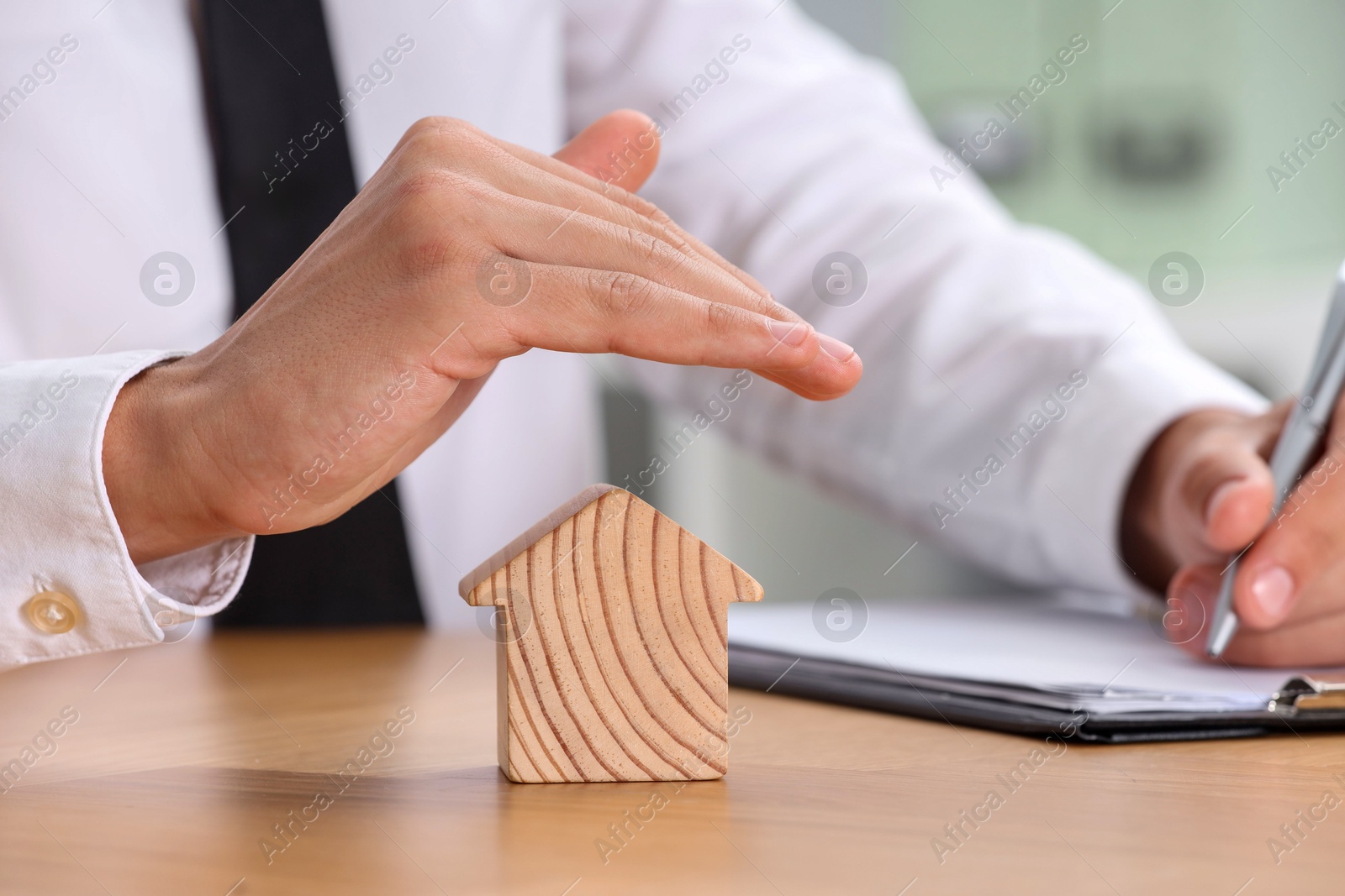 Photo of Property insurance. Real estate agent protecting house figure while working at wooden table, closeup