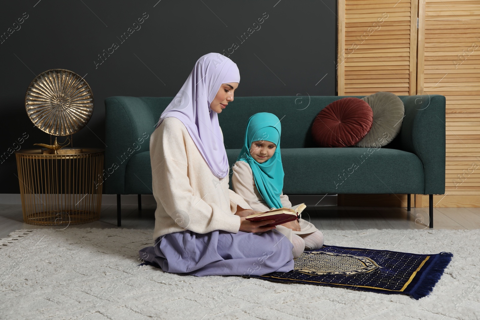 Photo of Muslim woman and her daughter with Quran praying on mat at home