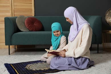 Photo of Muslim woman and her daughter with Quran praying on mat at home