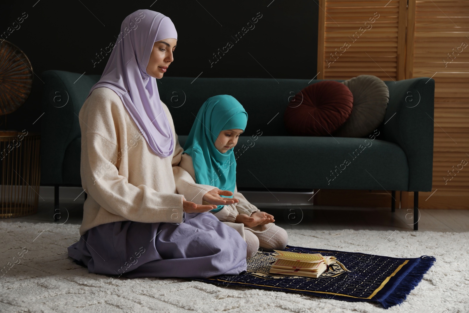 Photo of Muslim woman and her daughter with Quran praying on mat at home