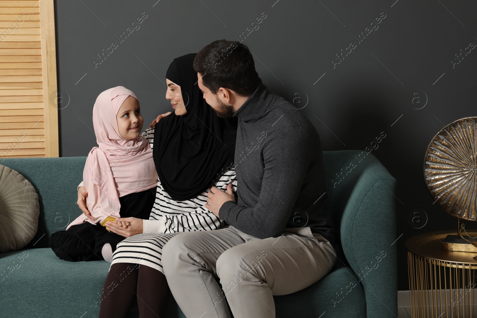 Photo of Happy Muslim family sitting on sofa at home