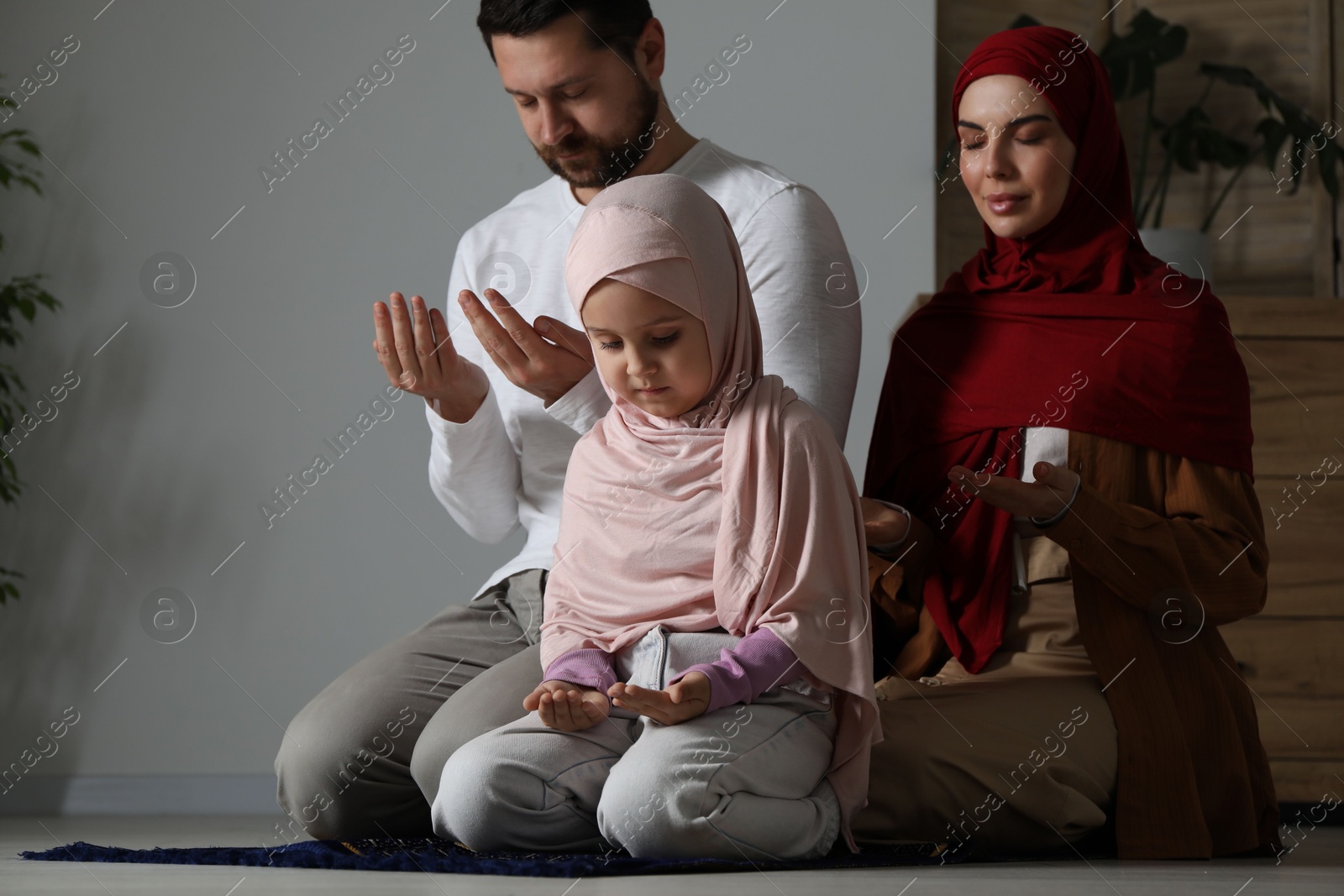 Photo of Muslim family praying on mat at home