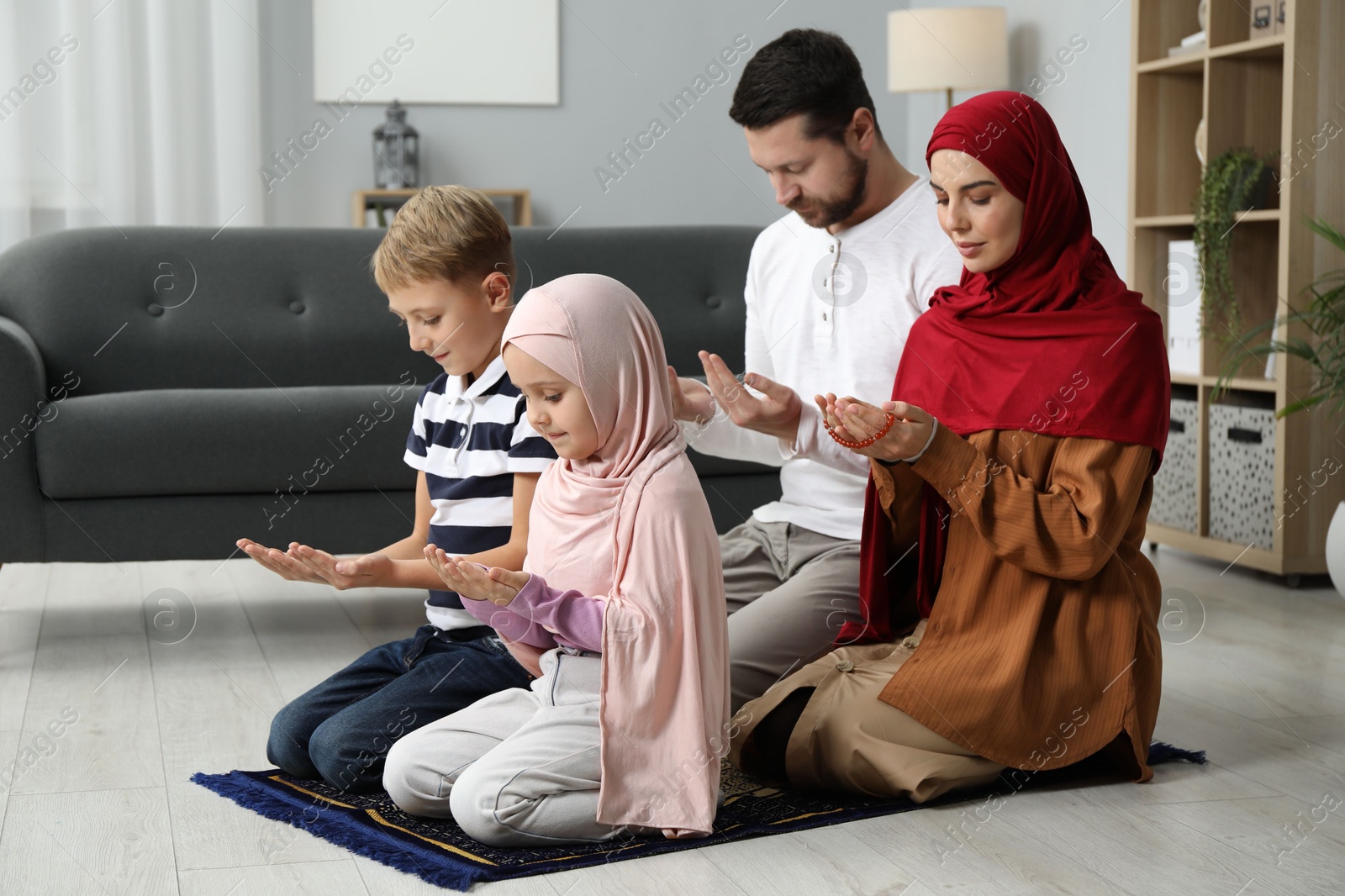 Photo of Happy Muslim family praying on mat at home