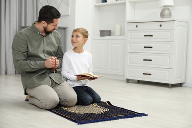 Photo of Muslim man with his son reading Quran and praying on mat at home, space for text