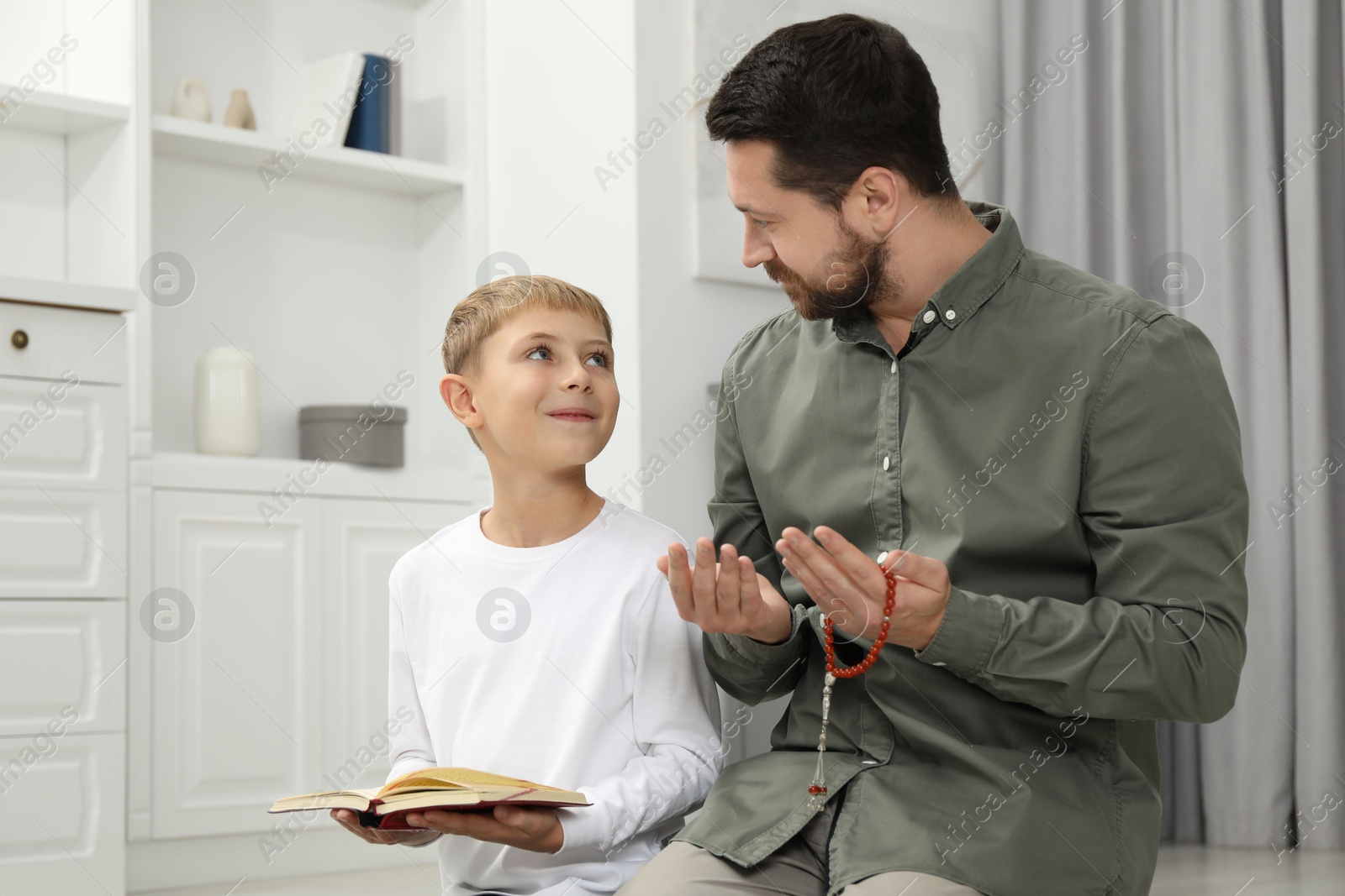 Photo of Muslim man with his son reading Quran and praying on mat at home