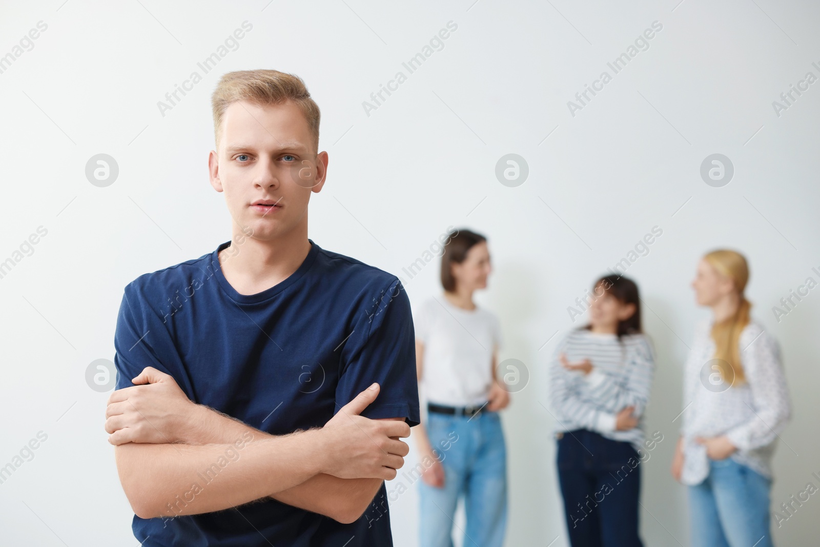 Photo of Young man feeling uncomfortable among people indoors, selective focus