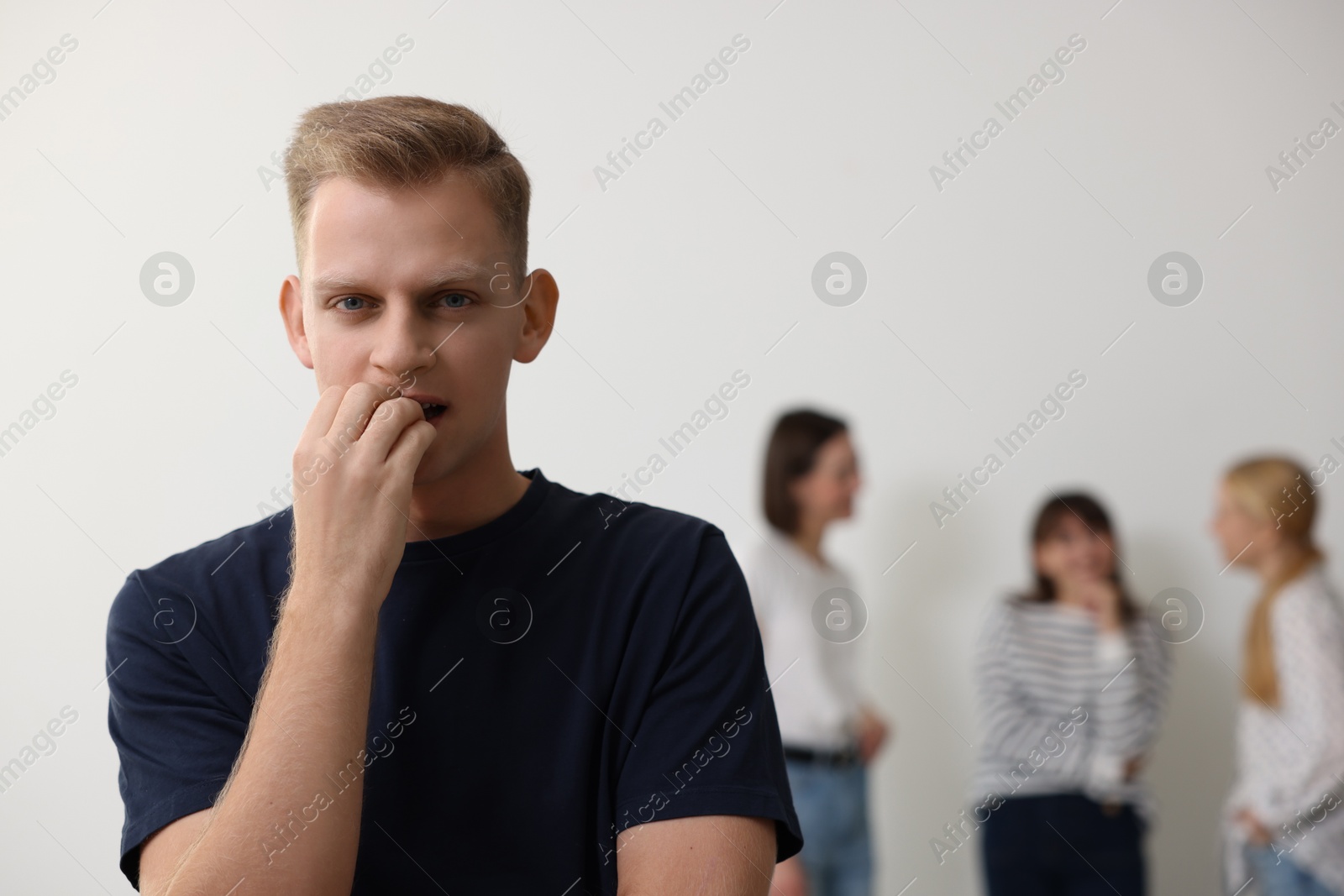 Photo of Young man feeling uncomfortable among people indoors, selective focus