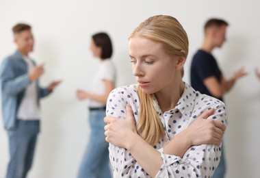 Photo of Young woman feeling uncomfortable among people indoors, selective focus