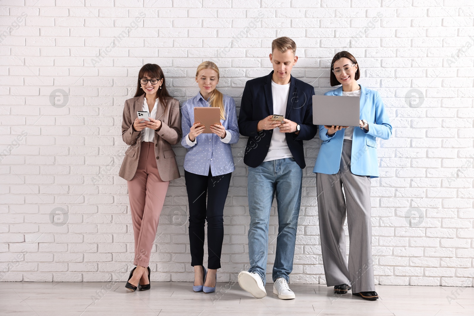 Photo of Group of people using different gadgets near white brick wall indoors. Modern technology