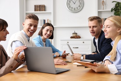 Photo of Group of people using different gadgets at wooden table in office. Modern technology