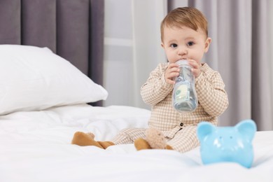 Photo of Cute little baby with money in bottle and piggybank on bed at home. Space for text