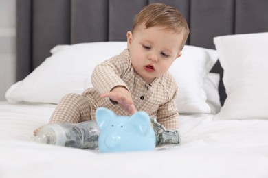 Photo of Cute little baby with money in bottle and piggybank on bed at home