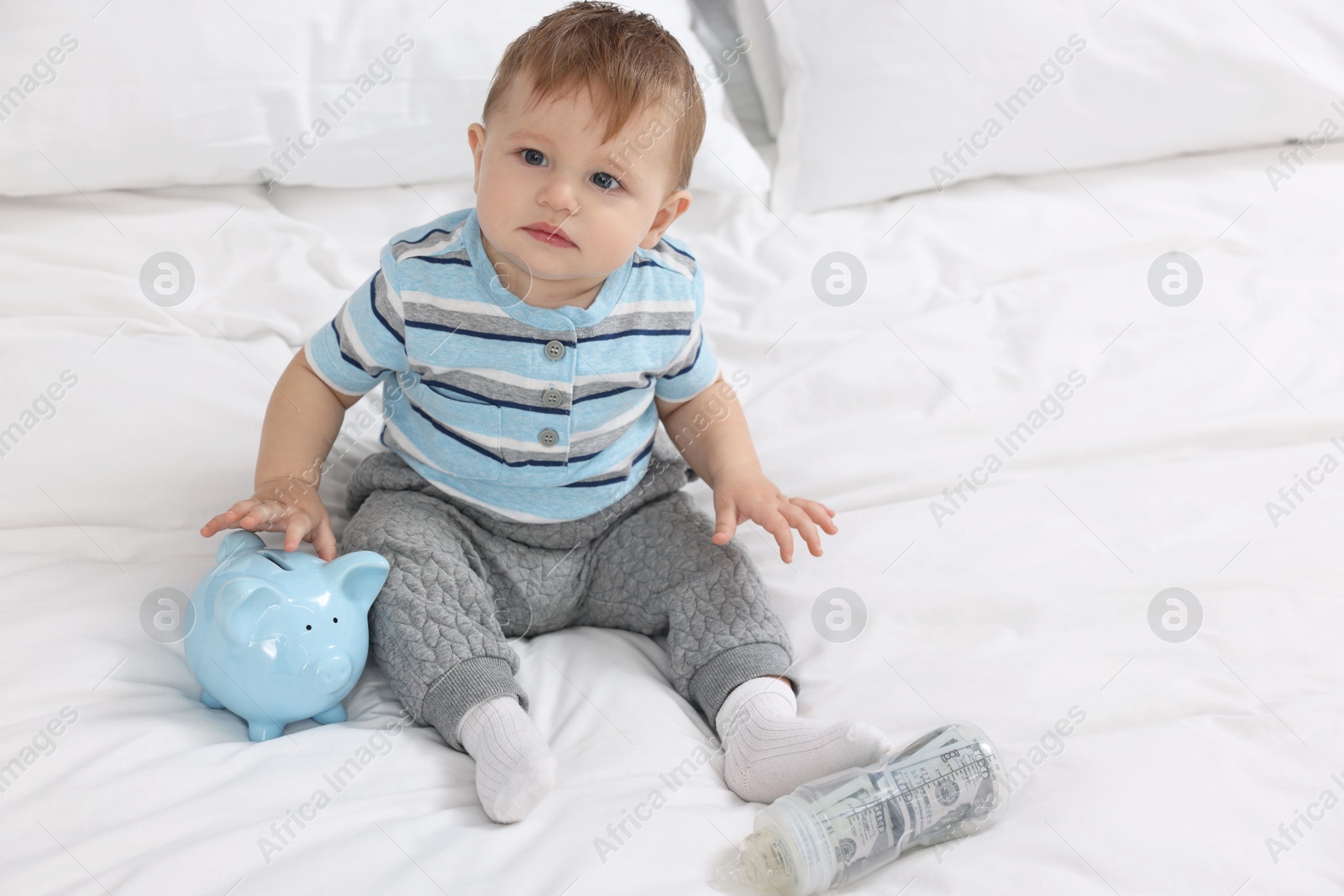 Photo of Cute little baby with money in bottle and piggybank on bed at home. Space for text