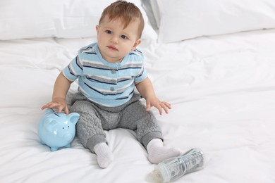 Photo of Cute little baby with money in bottle and piggybank on bed at home. Space for text