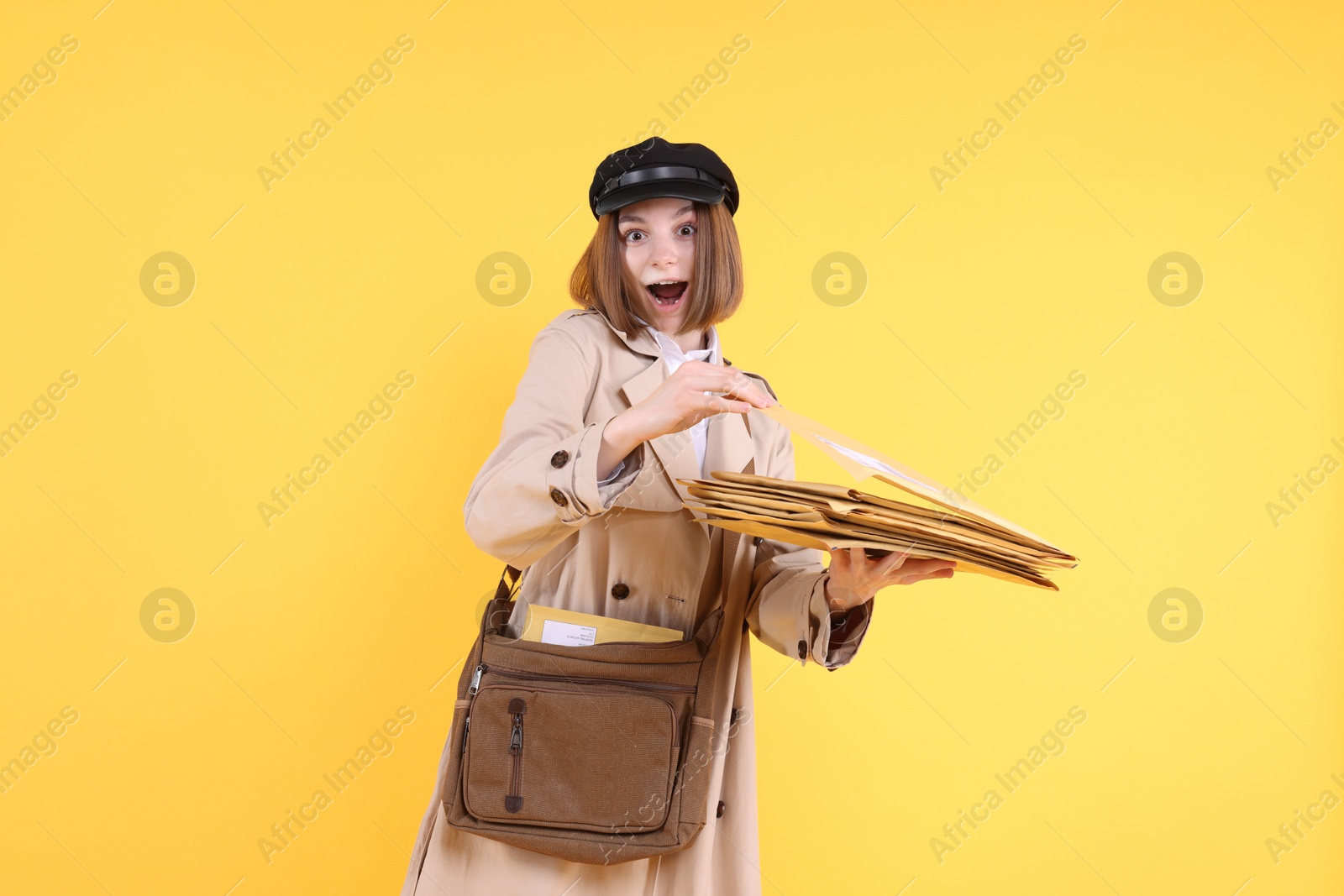 Photo of Emotional postwoman with bag and envelopes on yellow background