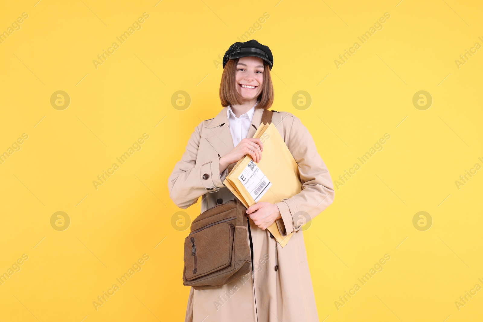 Photo of Happy postwoman with bag and envelopes on yellow background