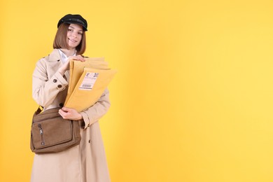 Photo of Happy postwoman with bag and envelopes on yellow background. Space for text