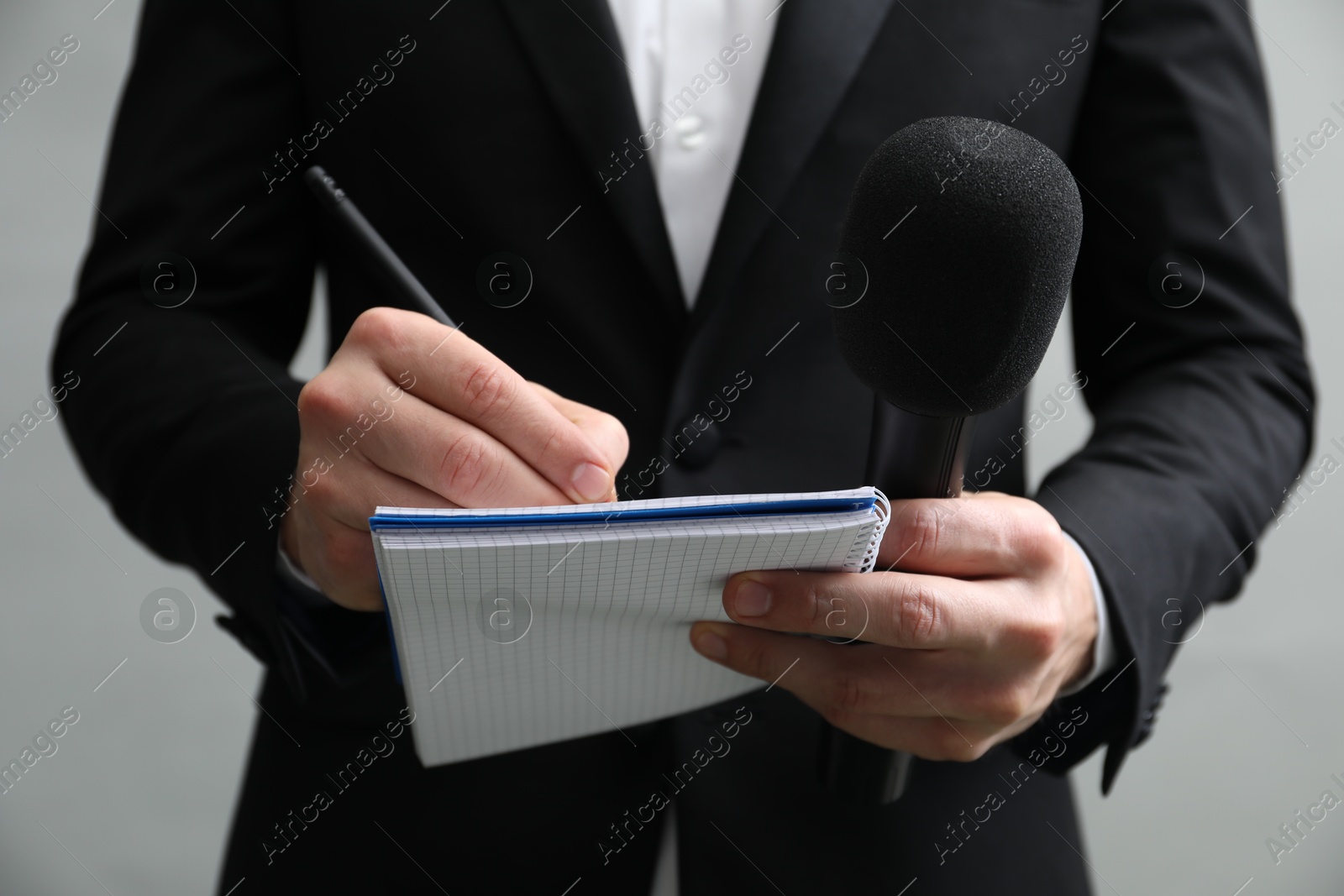 Photo of Journalist with microphone taking notes on grey background, closeup