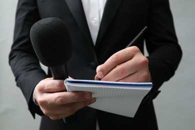 Photo of Journalist with microphone taking notes on grey background, closeup