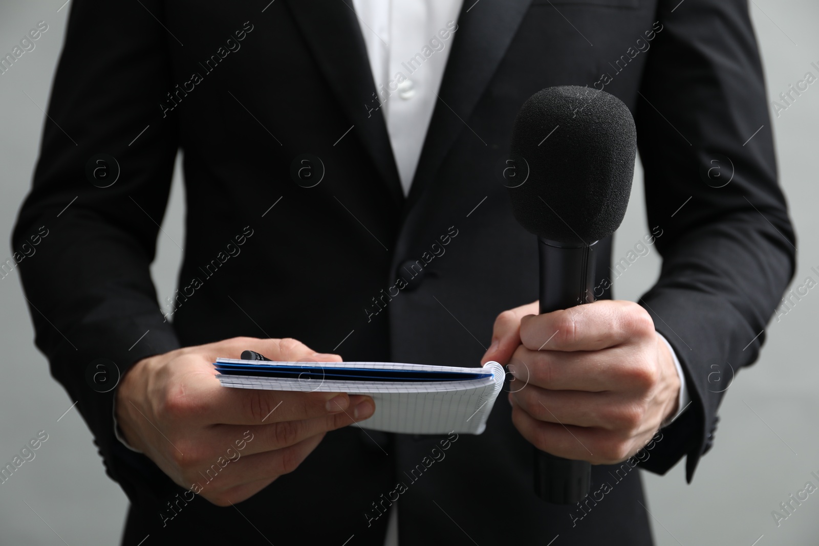 Photo of Journalist with microphone and notebook on grey background, closeup