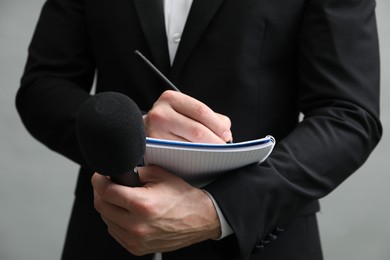 Photo of Journalist with microphone taking notes on grey background, closeup