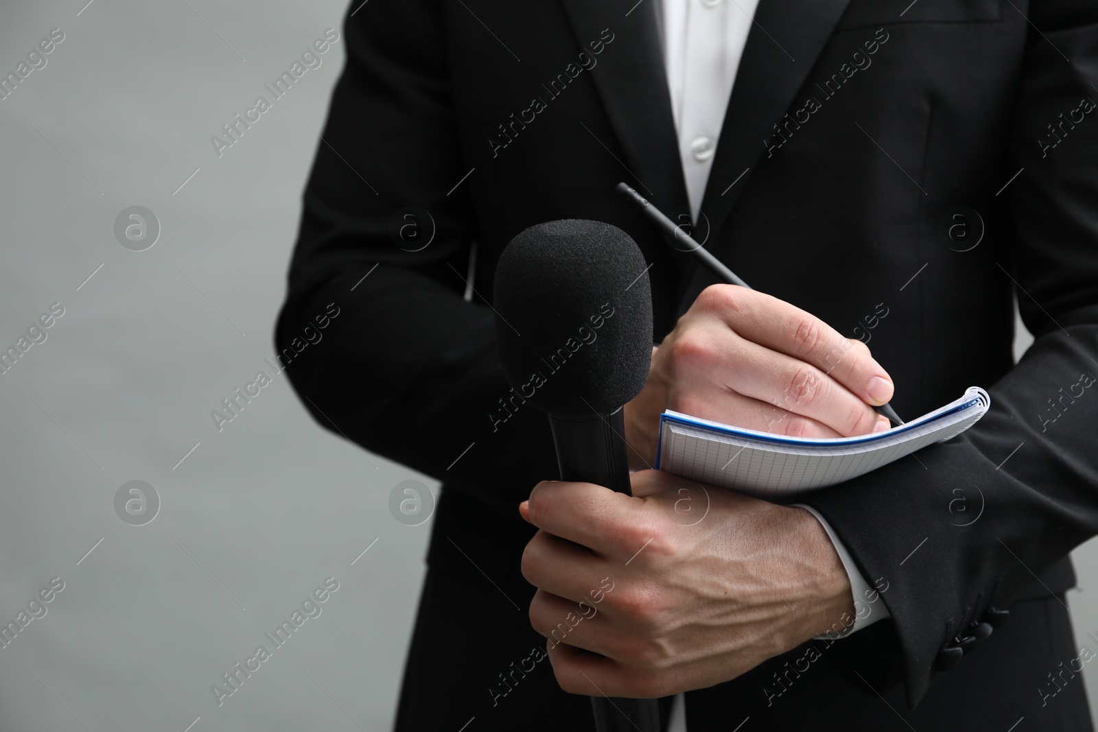 Photo of Journalist with microphone taking notes on grey background, closeup. Space for text