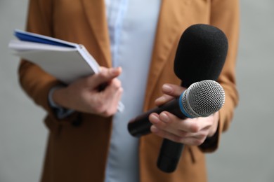 Photo of Journalist with microphones and notebook on grey background, closeup