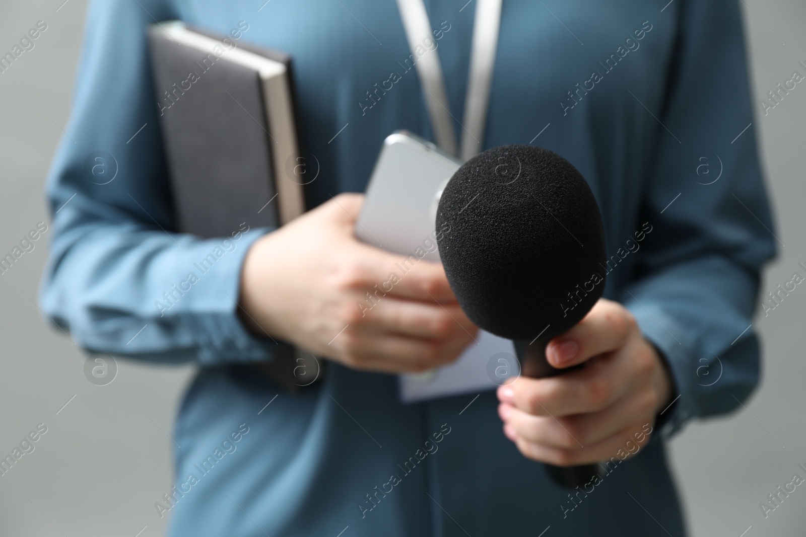 Photo of Journalist with microphone, smartphone and notebook on grey background, closeup