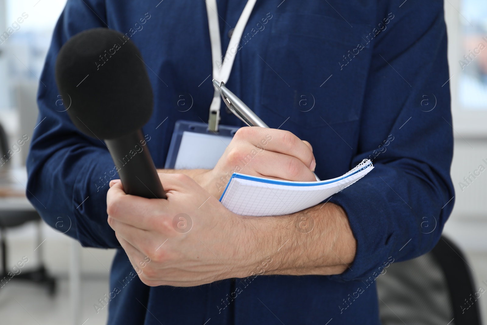 Photo of Journalist with microphone taking notes indoors, closeup