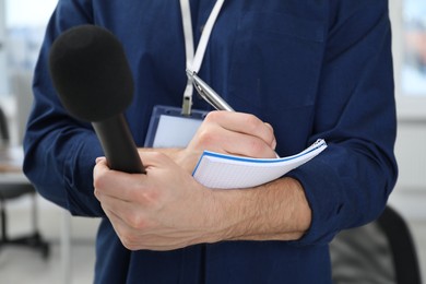 Photo of Journalist with microphone taking notes indoors, closeup