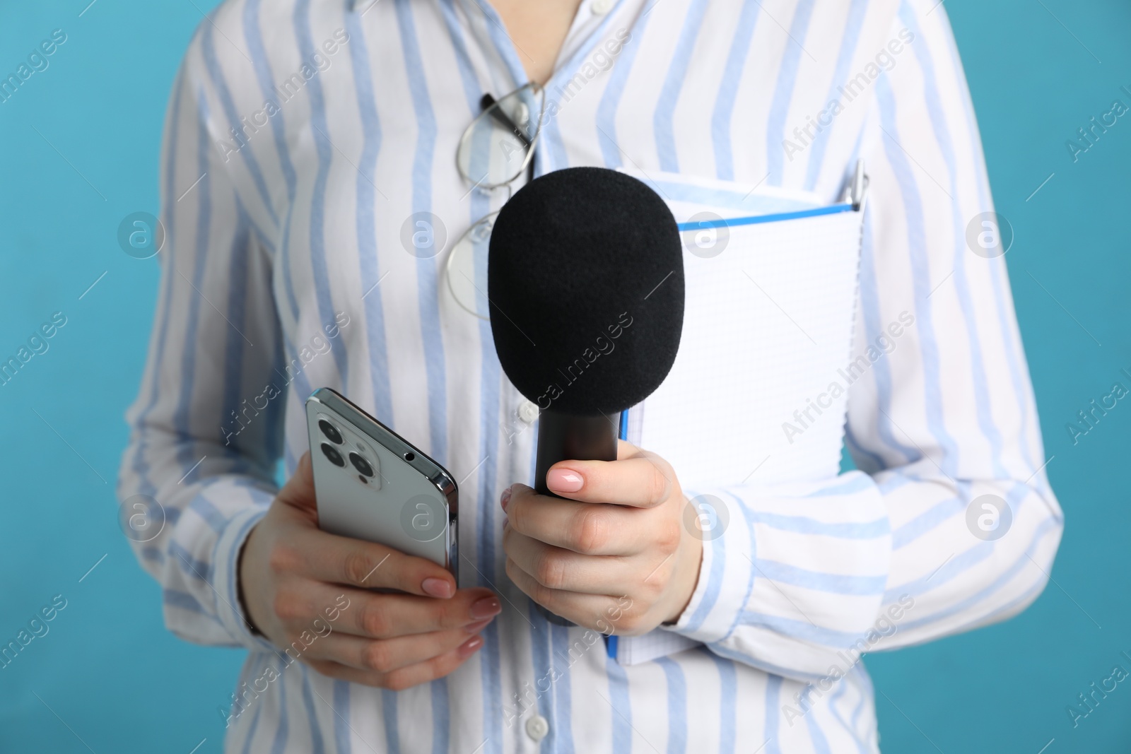 Photo of Journalist with microphone, notebook and smartphone on light blue background, closeup