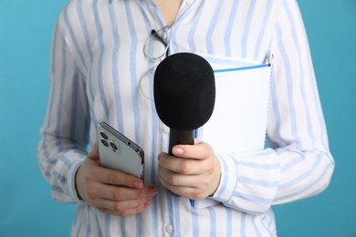 Photo of Journalist with microphone, notebook and smartphone on light blue background, closeup