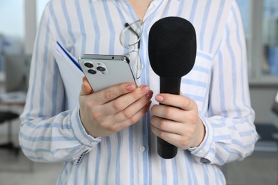 Photo of Journalist with microphone, notebook and smartphone indoors, closeup