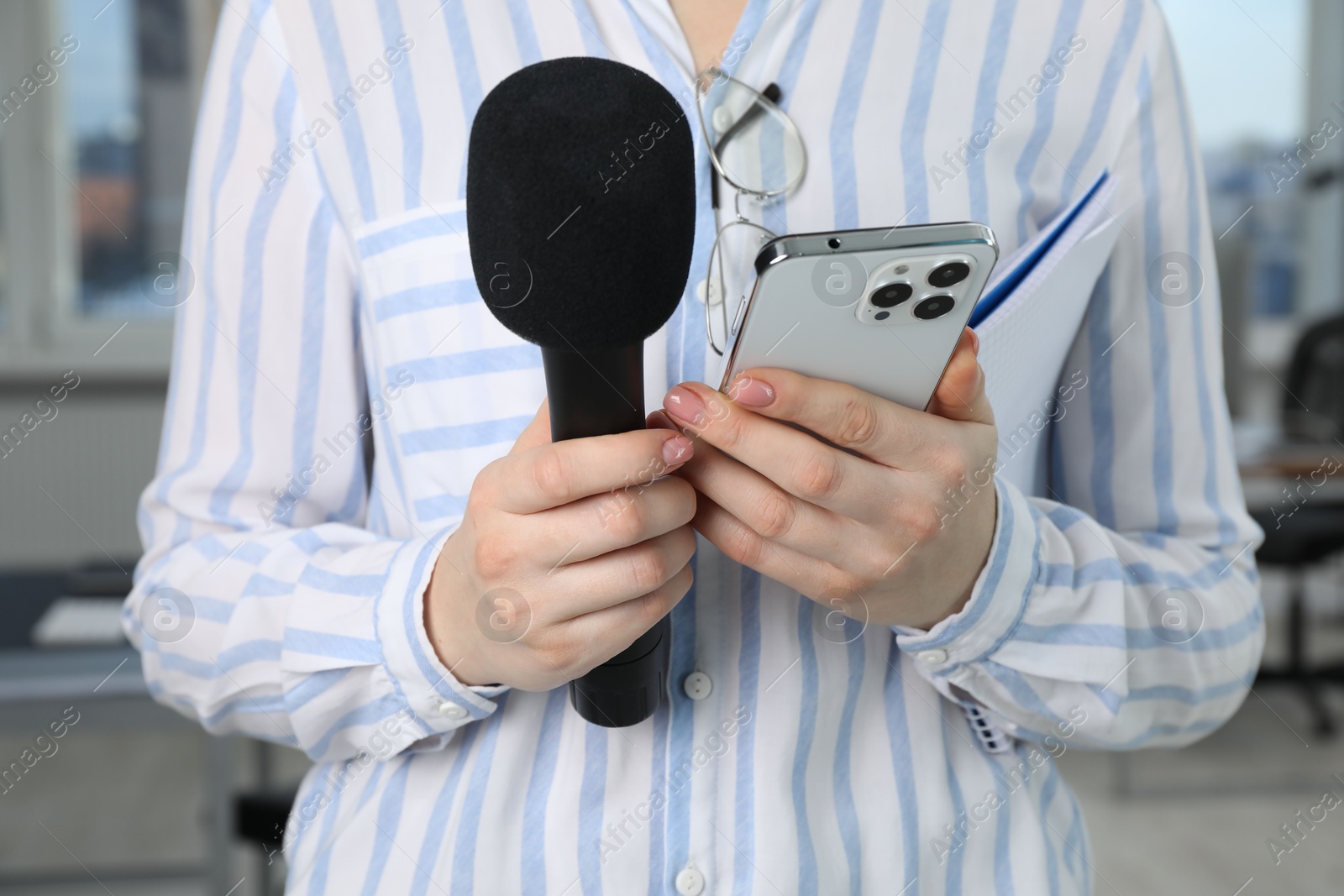 Photo of Journalist with microphone, notebook and smartphone indoors, closeup