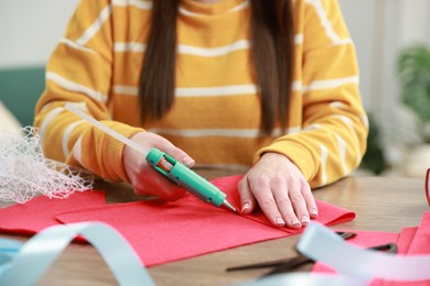 Photo of Woman with hot glue gun making craft at table indoors, closeup